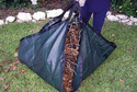 Picture of dark gray tarp on green gras filled with leaves & folded up at 4 courners ready to carry by handles