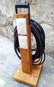 Vertical 2x4 with 2 electrical sockets - a handle - and a length of electrical cord on the back fastened to wood base