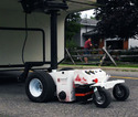 A white and red Remote-Controlled Trailer Mover hooked to a 5th-wheel style trailer