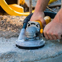 Angle grinder with a dust shroud and suction hose attached working on some cement