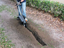 A person using a Handheld gas-powered trencher to cut a trench