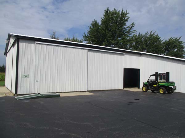 Pictured about to enter the smaller opening of a combination workshop/equipment-storage building is a UTV with items in its cargo bed.