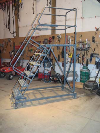 Pictured in a workshop is a five-steps-to- platform rolling ladder, which allows one to reach up to at least 12 feet; it includes safety railing both up the steps and around the platform.