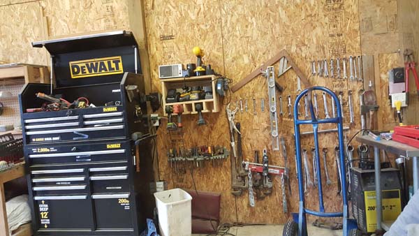 Pictured is a portion of a workshop’s plywood wall with numerous tools and tool-holding items hung on it.