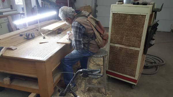 Pictured directly behind an adult male busy at a table in his workshop is a 5-foot-tall, stacked-filter air cleaning system unit.