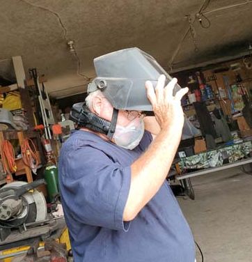 Pictured is an adult male in the process of slipping a powered air purifying filtered respirator mask down over his face.