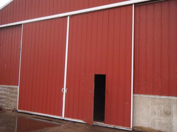 Pictured is a farm building’s large double sliding door (closed), one panel of which includes a walk-through door.