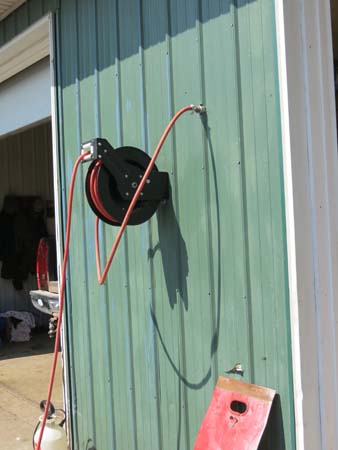 Pictured is an auto-rewind air hose reel mounted on the outside wall of farm building. 