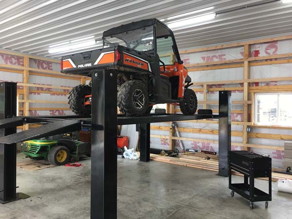 Pictured in the shop’s vehicle service/maintenance area is a vehicle hoist with a UTV aboard; a rolling tool cart is nearby.