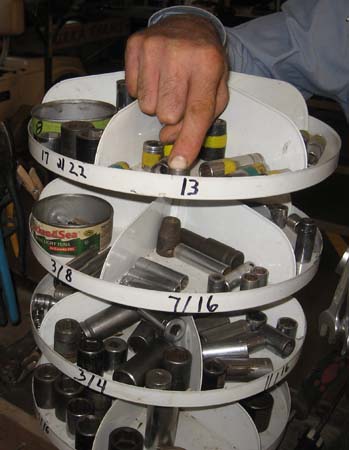 Pictured is an adult male’s hand removing an item from a round, rotatable, four-level tool tray, each tray having four sections,