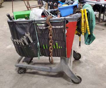 Pictured is a 3-foot-high, four-sided plastic tool cart; hanging over the exterior of each of the sides are pocketed fabric ‘aprons’ with various tools in the pockets.