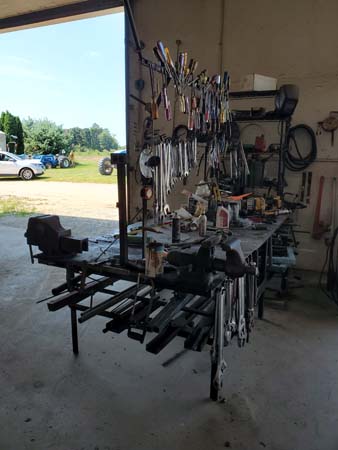 Pictured is a 4-foot-long, 3-foot-deep, 2.5-foot-tall movable workbench with a framed height extension housing many hanging tools and numerous other tools/items on the bench surface.