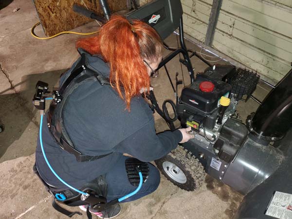 Woman wearing upper body exoskeleton kneeling to work on rototiller