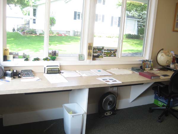 Pictured to accommodate a wheelchair user in his farm office is a long, against-the-wall, roll-under desk with four vertical windows immediately above the desk.