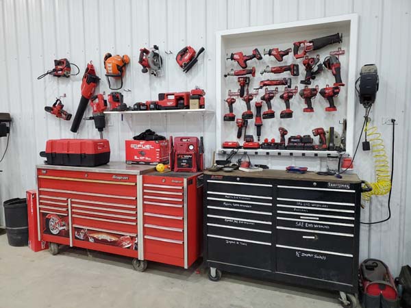 Pictured are side-by-side wheeled hardware-drawer cabinets above which, on the wall behind (either hung or on shelve), are many and varied battery-powered hand tools.